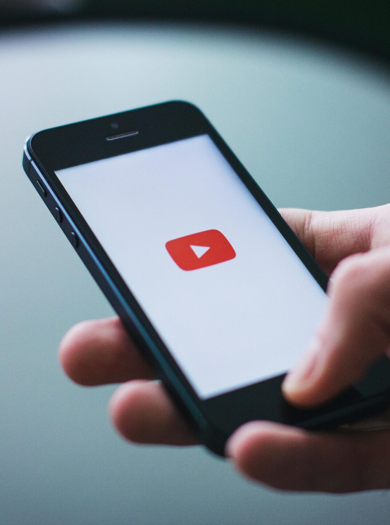 Recursos Close-up of a hand holding a smartphone displaying the YouTube app on the screen.